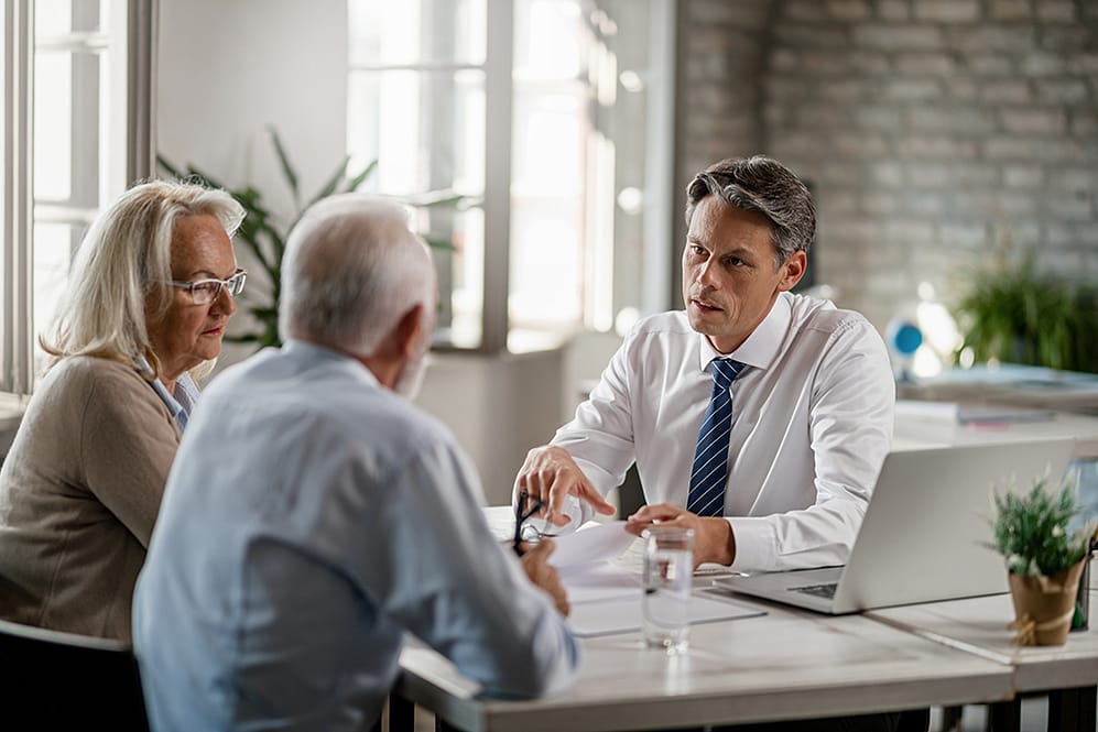 Financial advisor and senior couple talking while going through paperwork on a meeting.